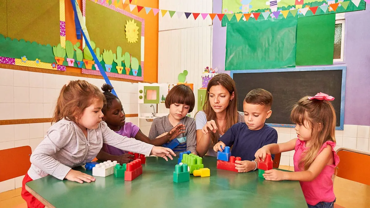 An educator building with blocks alongside a group of children at a table