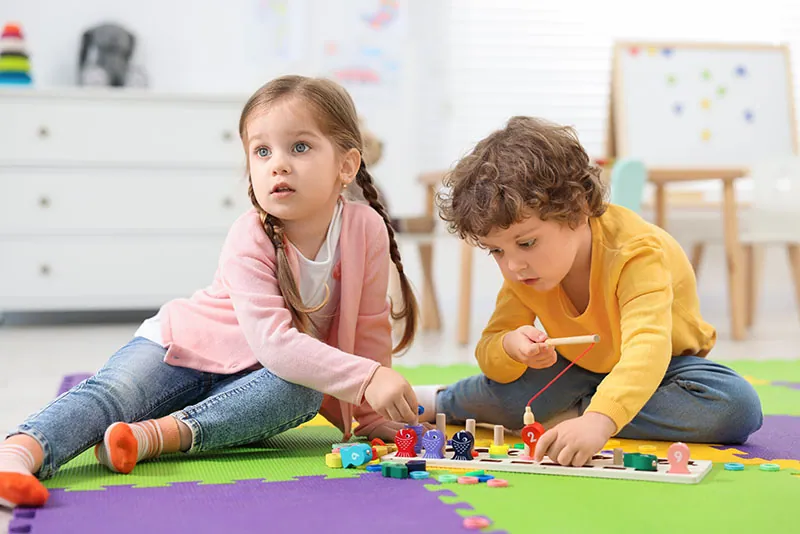 Two children playing with wooden number toys on a colourful play mat