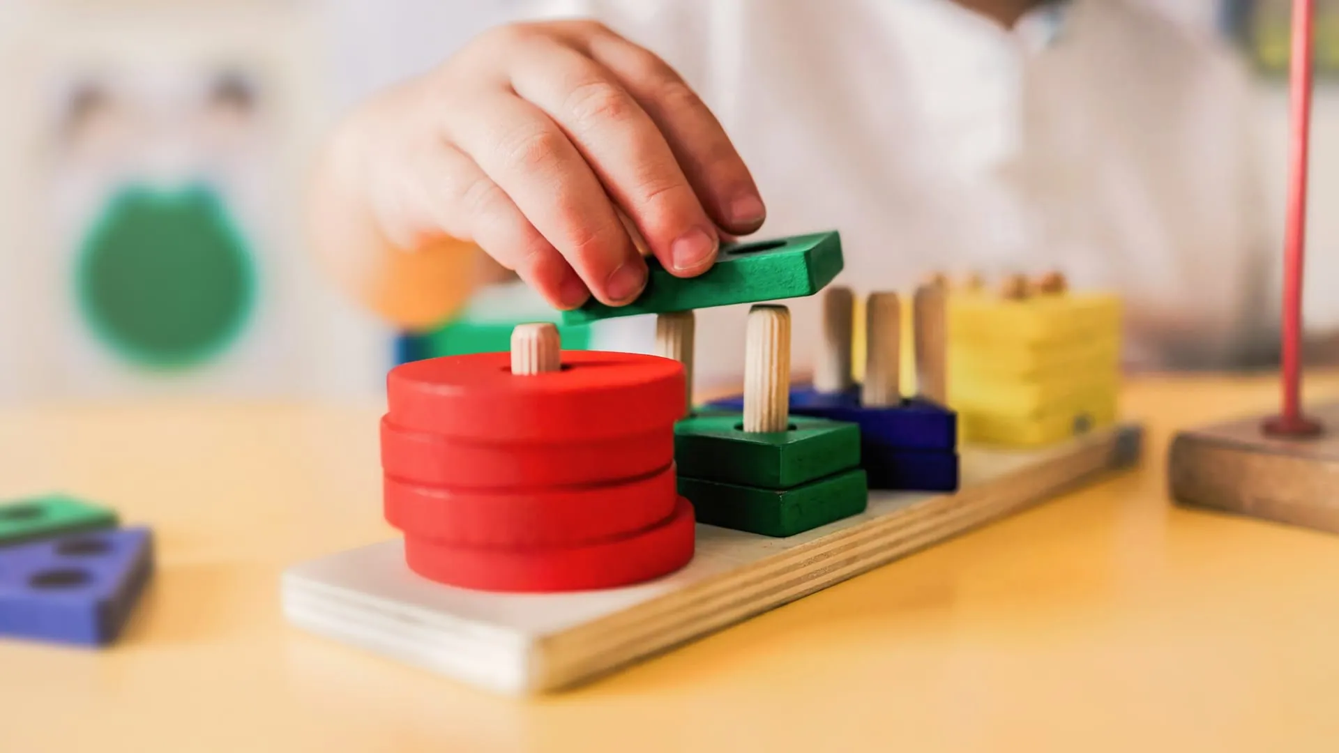 Child stacking colorful shape blocks on wooden pegs